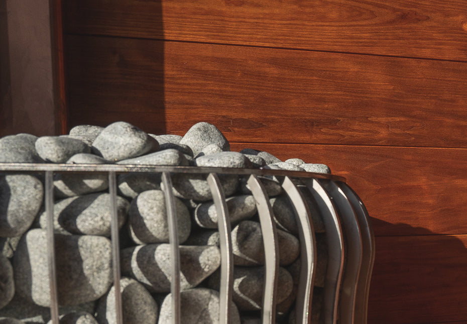 The metal basket of the sauna stove is filled with polished gray stones
