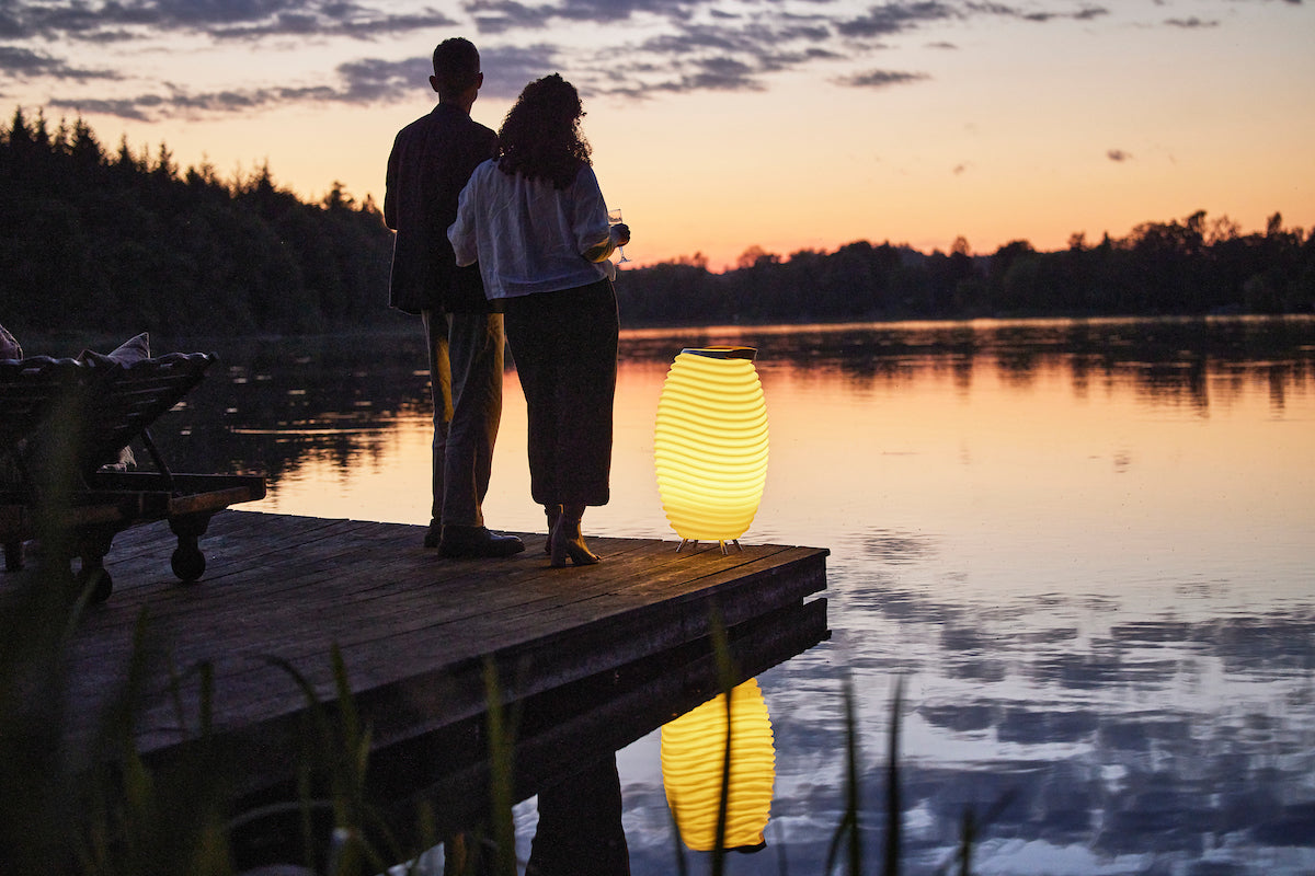 Portative Kooduu lamp, creates a romantic atmosphere for a couple standing on a pier and enjoying an evening view of the lake