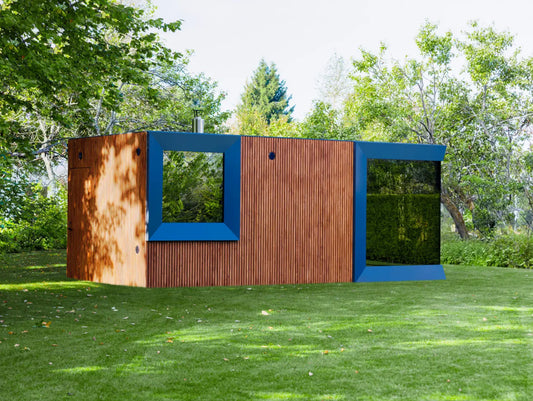 Modern outdoor sauna with wooden panels and blue accents in a green, tree-filled landscape.